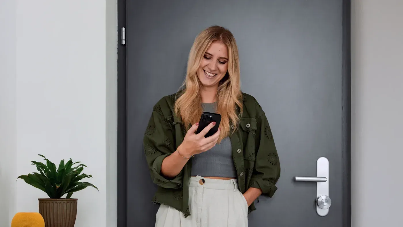 Nuki Smart Lock Pro posée sous la béquille d'une porte grise, commandée depuis un téléphone
